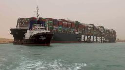 In this photo released by the Suez Canal Authority, a boat navigates in front of a massive cargo ship, named the Ever Green, rear, sits grounded Wednesday, March 24, 2021, after it turned sideways in Egypt's Suez Canal, blocking traffic in a crucial East-West waterway for global shipping. An Egyptian official warned Wednesday it could take at least two days to clear the ship. (Suez Canal Authority via AP)