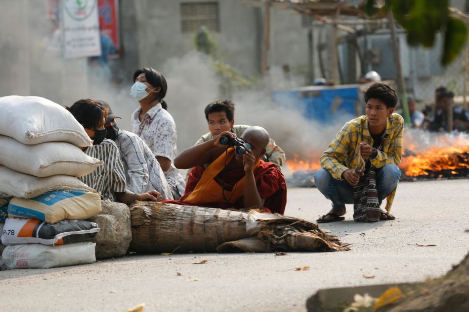 A Buddhist monk uses binoculars as he squats behind a road barricade with others in Mandalay, Myanmar, on March 22.