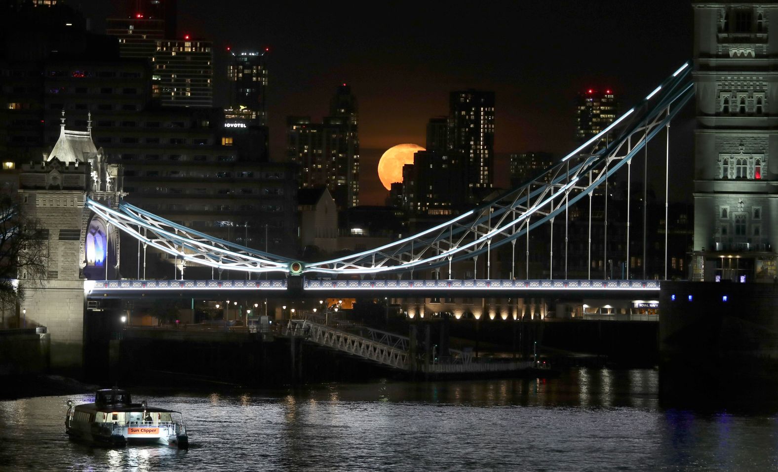 The moon appears between buildings behind Tower Bridge in Central London on Monday.