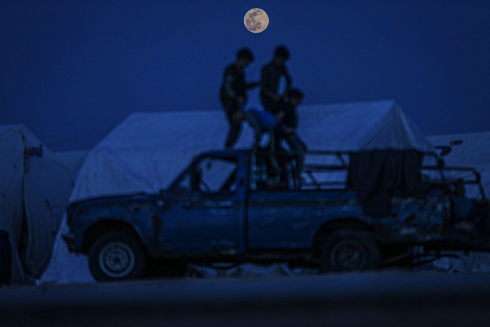 Syrian kids stand on a vehicle under the moon at the Maarrat Misrin camp in Idlib province, Syria.