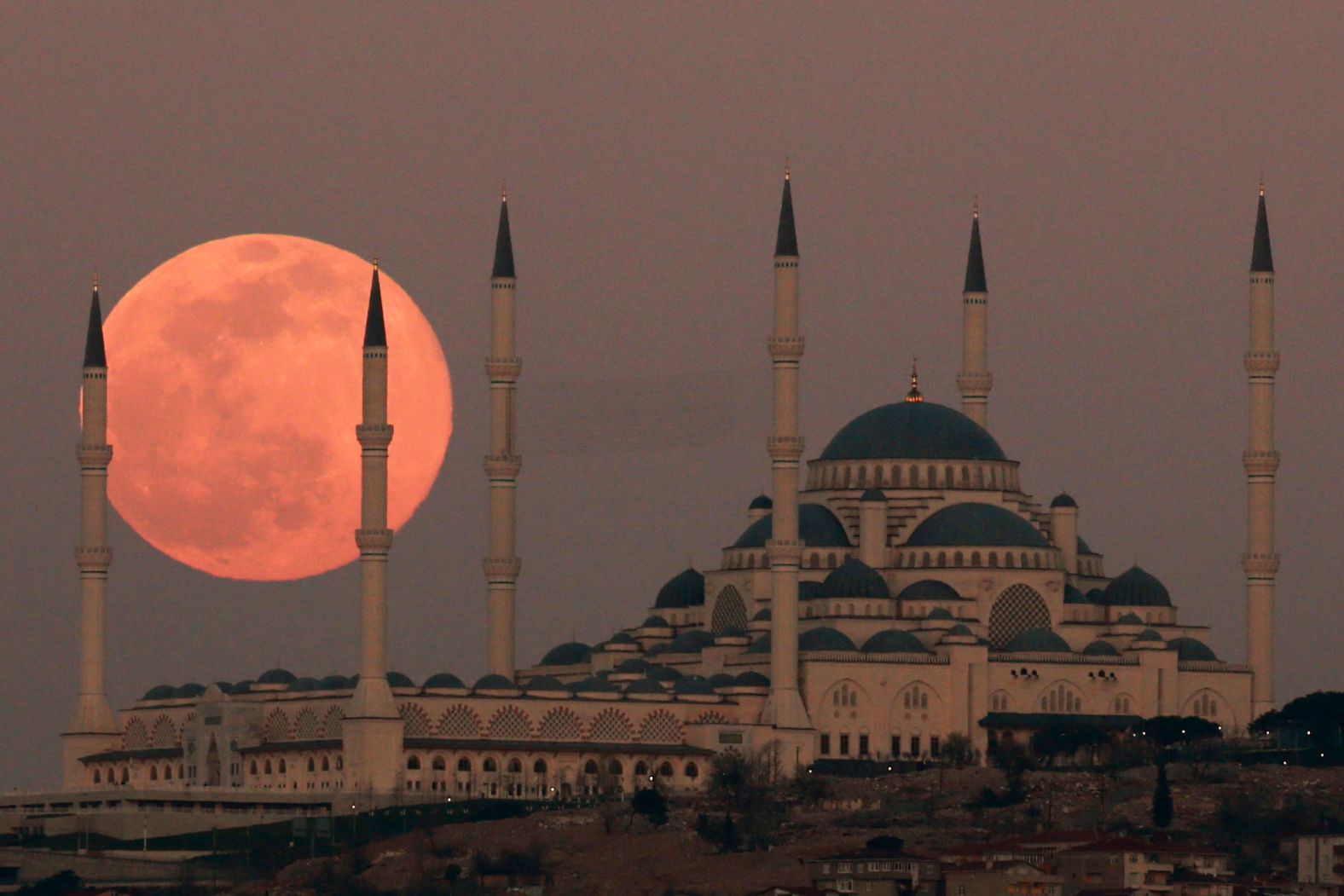 The moon is seen behind the Camlica Mosque in Istanbul, Turkey.