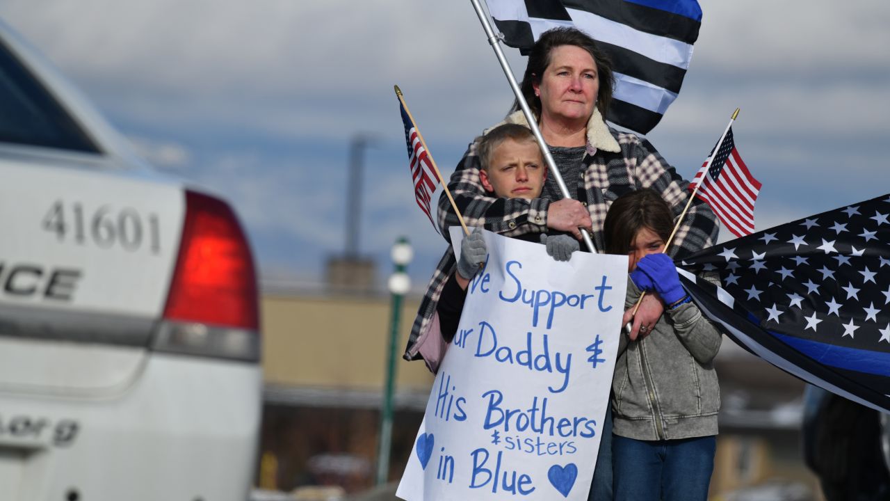 Vala Clark, center, with her grandchildren Wesley Haymore, 10, left, and his sister Andilyn, 7, waves flags for Officer Eric Talley in front of King Soopers on State Highway 7. 