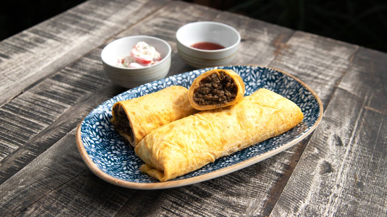 Singaporean beef murtabak is an egg crepe wrapped around ground beef served with fresh lime, chili sauce and raita.