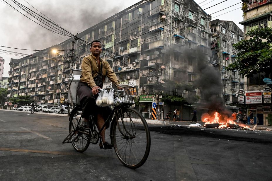 A man rides his bike as smoke billows from burning barricades in Yangon on March 30.