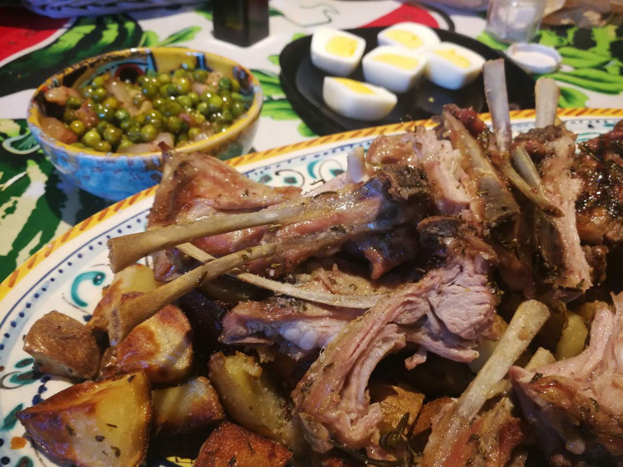 Lamb chops are traditionally served on Easter in Italy. In Florence, locals serve tiny lamb chops called scottadito, meaning finger-burners, because you burn yourself picking up the tiny bones to eat them. Behind the lamb is roasted potatoes, peas with pancetta and hard-boiled eggs.