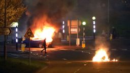 A man walks past a burning car that was hijacked by Loyalists at the Cloughfern roundabout in Newtownabbey, Belfast, Northern Ireland, Saturday April 3, 2021. Masked men threw petrol bombs and hijacked cars in the Loyalist area North of Belfast. Loyalists and unionists are angry about post-Brexit trading arrangements which they claim have created barriers between Northern Ireland and the rest of the UK.