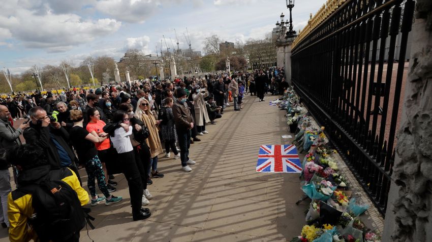People view flowers left in front of the gate at Buckingham Palace in London, after the announcement of the death of Britain's Prince Philip, Friday, April 9, 2021. Buckingham Palace officials say Prince Philip, the husband of Queen Elizabeth II, has died. He was 99. Philip spent a month in hospital earlier this year before being released on March 16 to return to Windsor Castle.