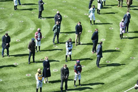 Jockeys and trainers stand for a minute of silence at the Grand National Festival in Liverpool, England.