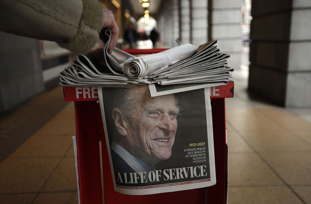 A person in London takes a copy of a newspaper with a Philip tribute on the front page.