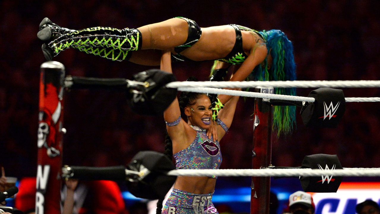 Bianca Belair (silver attire) holds Sasha Banks (black and green attire) over the ring during the championship match. 