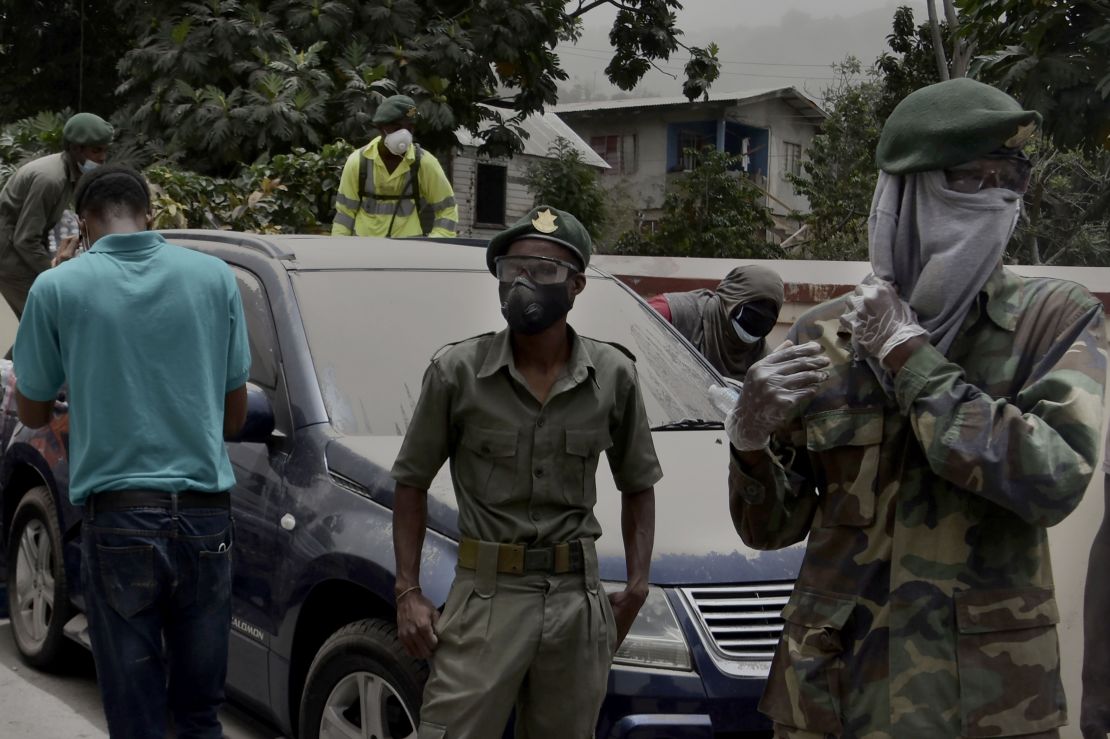 Soldiers and residents stand beside an ash-covered town in Kingstown, Saturday.