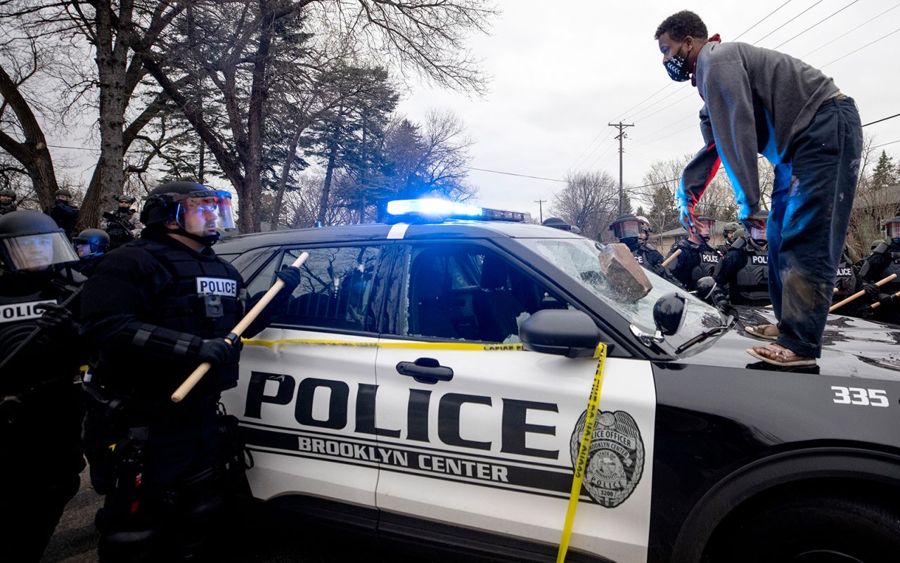 A man stands atop a police car after throwing a brick at its windshield on Sunday.