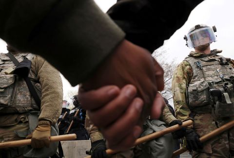 Members of the National Guard watch as protesters hold hands during a rally outside the Brooklyn Center Police Department on Monday.