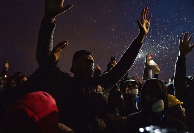 Protesters raise their hands in front of the Brooklyn Center Police Department on Monday.