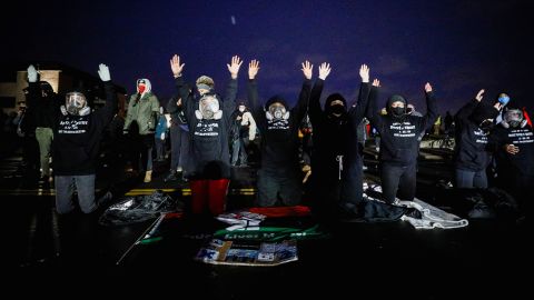 Activists raise their arms as they confront State troopers, National Guard members and other law enforcement officers following a march for Daunte Wright, 20, who was shot and killed by former Brooklyn Center Police Officer Kim Potter.
