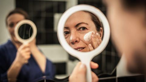 Productos para combatir el acné aprobados por dermatólogos - Mujer aplicando crema facial en el espejo