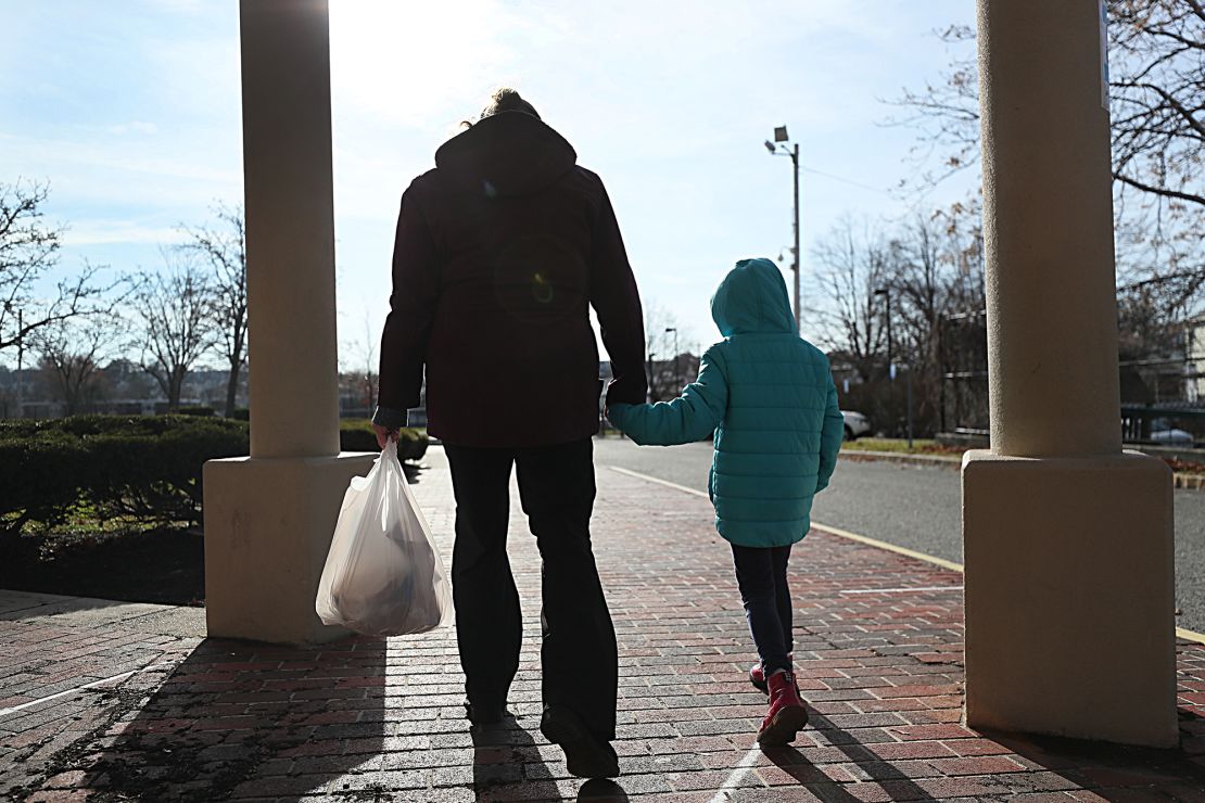 A woman and her daughter walk from  her elementary school after picking  up her breakfast and lunch in Revere, MA on Dec. 11, 2020. She is among many low-income parents in Massachusetts who have struggled to receive their promised free school meals during the pandemic. Her daughter's school offers meal pick-up from 10:30a.m. to 1 p.m., but her daughter only has a break from classes from 10:50 to 11:30, and so the single mother must strap her daughter in a jogging stroller and rush to the school a half-mile away since they don't have a car to pick up meals. (Photo by Suzanne Kreiter/The Boston Globe via Getty Images)