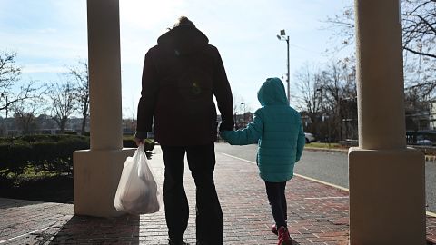 A woman and her daughter walk from  her elementary school after picking  up her breakfast and lunch in Revere, MA on Dec. 11, 2020. She is among many low-income parents in Massachusetts who have struggled to receive their promised free school meals during the pandemic. Her daughter's school offers meal pick-up from 10:30a.m. to 1 p.m., but her daughter only has a break from classes from 10:50 to 11:30, and so the single mother must strap her daughter in a jogging stroller and rush to the school a half-mile away since they don't have a car to pick up meals. (Photo by Suzanne Kreiter/The Boston Globe via Getty Images)