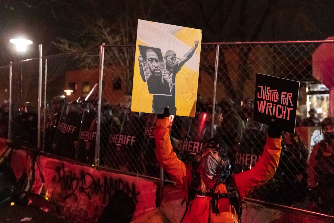 A demonstrator holding a poster of George Floyd and sign reading "Justice for Wright" in front of a line of police officers outside the Brooklyn Center police building.