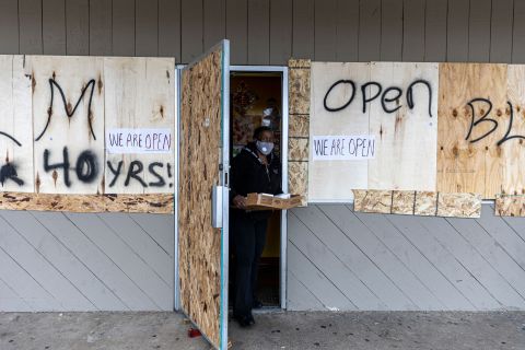A customer steps out of a store Wednesday that was boarded up as a result of the previous night's unrest.