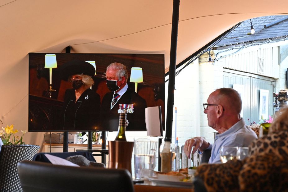 Prince Charles and his wife, Camilla, the Duchess of Cornwall, are seen on television as people watch the funeral from a pub in Winkfield, England.