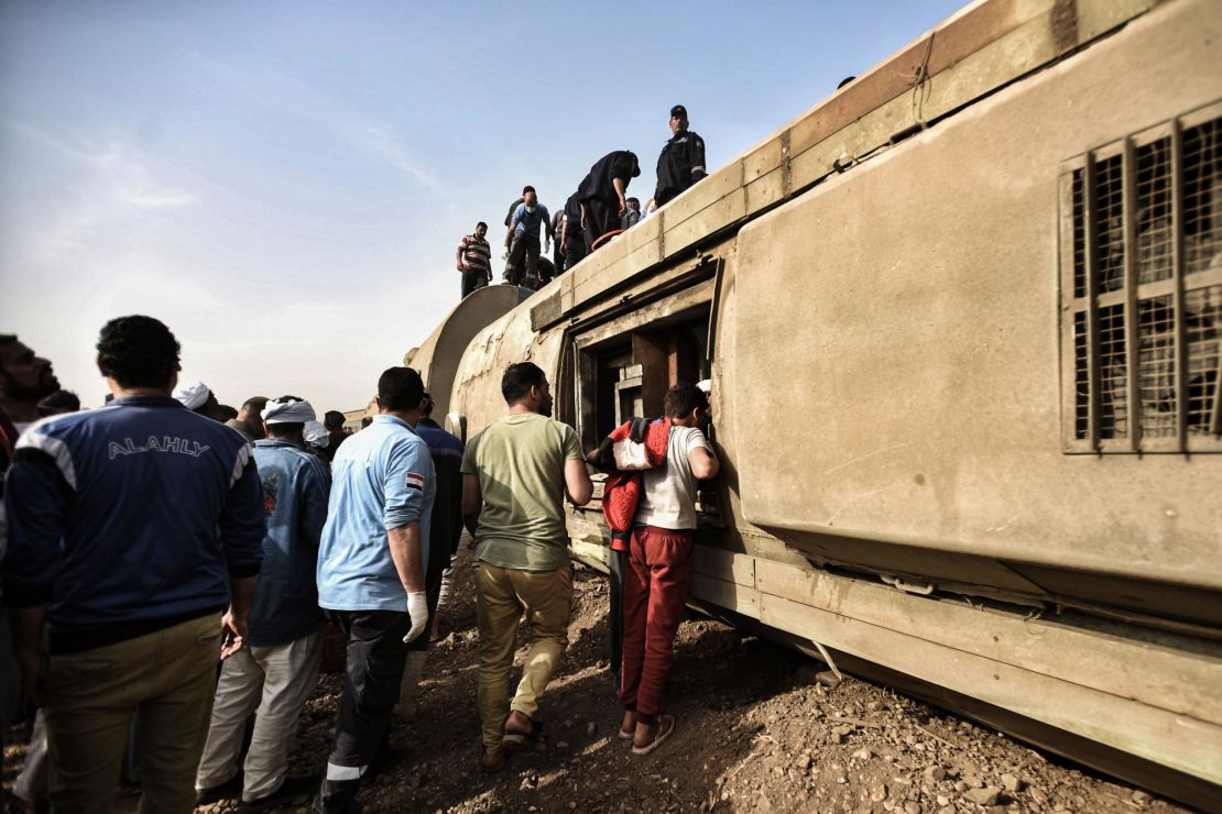 People inspect the damaged wagons of a passenger train, which went off the tracks near Toukh.