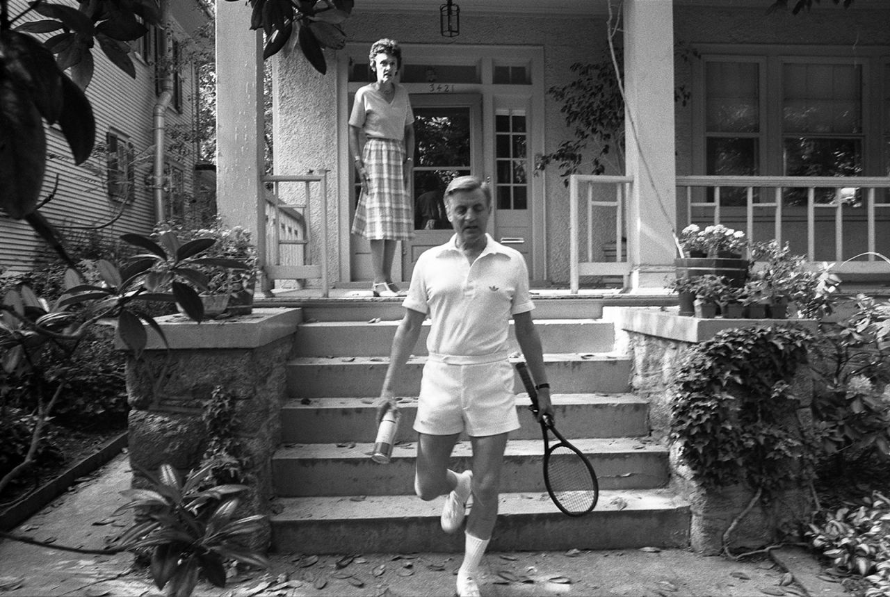 Mondale heads out to play tennis while his wife Joan stands on the porch of their Washington, DC, home in 1983.