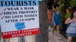 Tourists without face masks walk past a sign in the tourist zone of El Condado in San Juan, Puerto Rico on March 14, 2021. (Photo by Ricardo ARDUENGO / AFP) (Photo by RICARDO ARDUENGO/AFP via Getty Images)