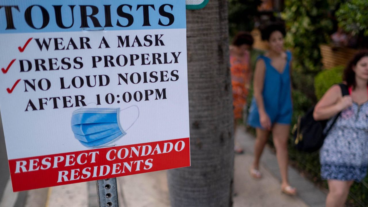 Tourists without face masks walk past a sign in the tourist zone of El Condado in San Juan, Puerto Rico on March 14.