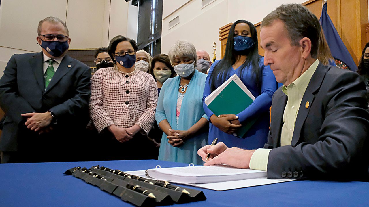 Virginia Gov. Ralph Northam puts his name to one of the marijuana legalization bills he signed at a ceremony inside the Patrick Henry Building in Richmond, Virginia, on April 21, 2021. Looking on, from left, are: state Sen. Adam Ebbin, Sen. Jennifer McClellan, Sen. Louise Lucas, and House Majority Leader Charniele Herring.