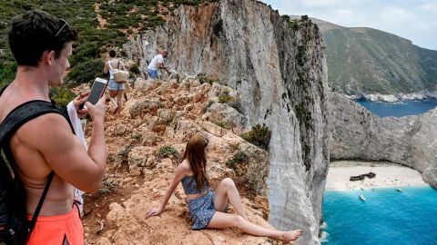 Tourists take pictures and selfies from a rock overlooking the famous Navagio (Shipwreck) beach on the Ionian island of Zakynthos on July 18, 2020. - Usually for the season, there is 20 daily departures for the island's landmark beach, now only four operate daily. (Photo by Louisa GOULIAMAKI / AFP) (Photo by LOUISA GOULIAMAKI/AFP via Getty Images)
