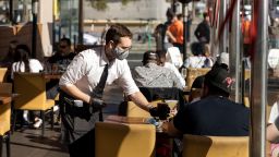 A waiter wearing a protective mask serves a drink at a restaurant on Ocean Ave. in Los Angeles, California, U.S. on Thursday, April 8, 2021. California officials plan to fully reopen the economy on June 15, if the pandemic continues to abate, after driving down coronavirus case loads in the most populous U.S. state. Photographer: Roger Kisby/Bloomberg via Getty Images