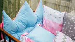 Cots and pillows and bumpers of different colors. Turquoise pillow, crown, grey, pink and turquoise pillows with geometric patterns.