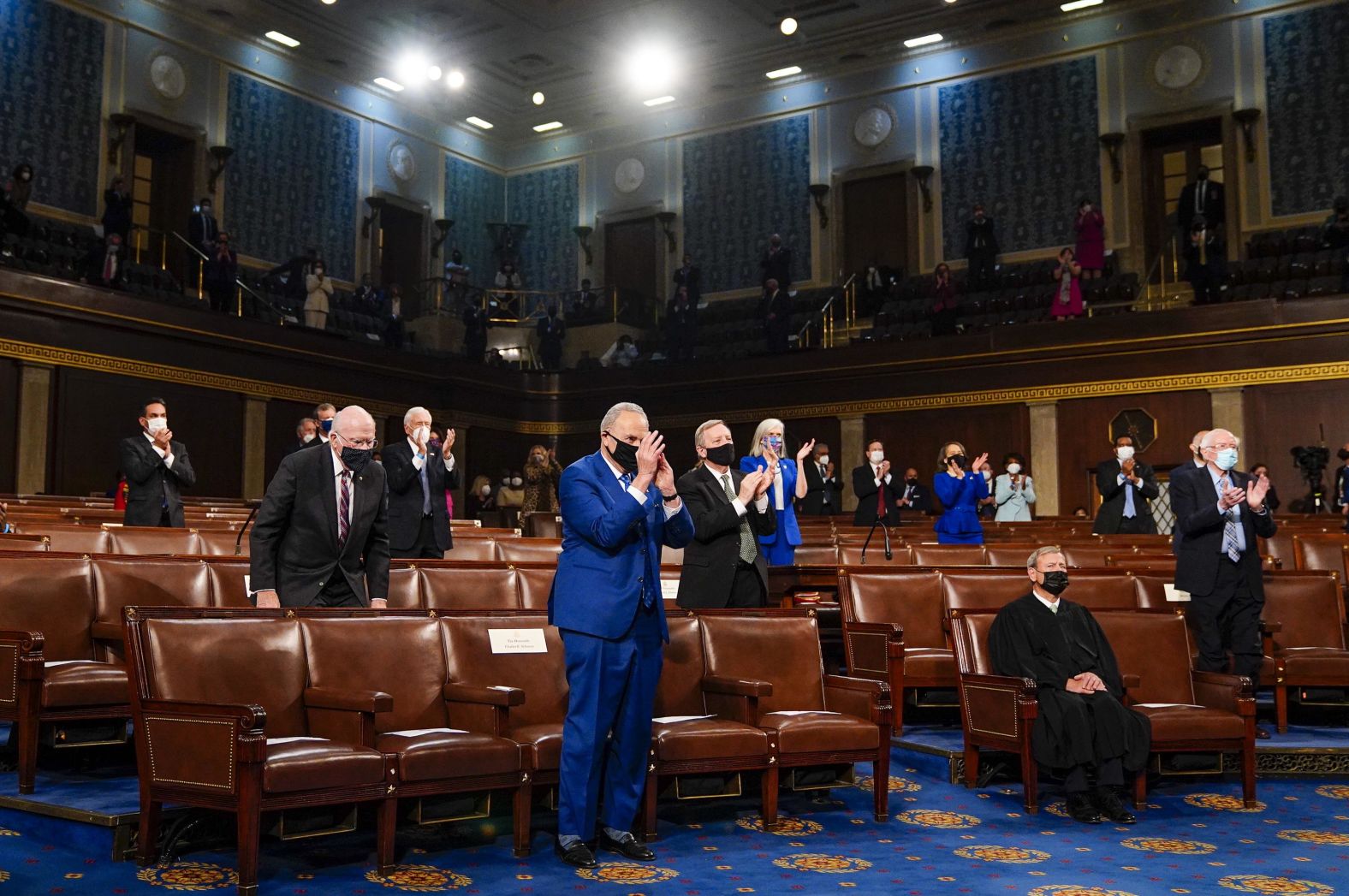 Senate Majority Leader Chuck Schumer applauds Biden from the front row.