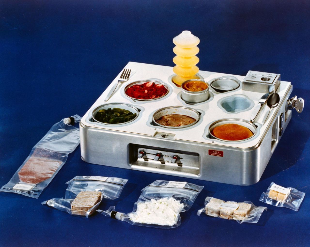 This food tray was used in the now-defunct Skylab, the first US space station launched by NASA in 1973. Shown in the tray are (counterclockwise from back): orange drink, strawberries, asparagus, prime rib, dinner roll and  butterscotch pudding.