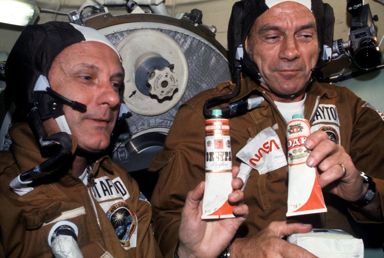 NASA Astronauts Thomas P. Stafford (left) and Donald K. "Deke" Slayton (right) hold containers of Soviet space food in the Soyuz Orbital Module during a nine-day joint US-USSR space mission in July 1975. The containers -- over which vodka labels have been pasted -- hold borscht (beet soup). This was the crews' way of toasting each other.