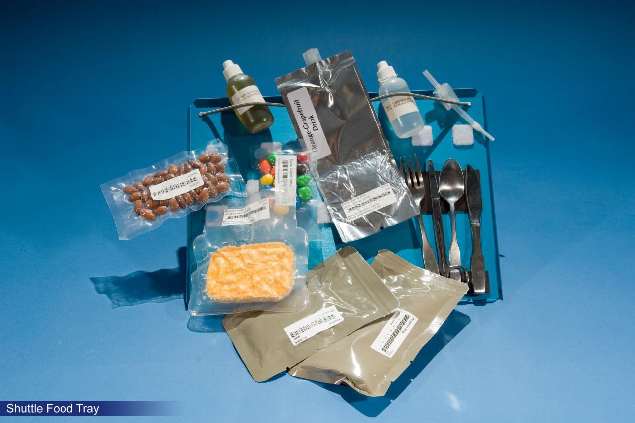 Shown are rehydratables from the '80s Space Shuttle missions and the first appearance of M&Ms on the space food menu. Referred to simply as "candy-coated chocolates" by NASA, they are now a regular space snack. Note the magnets securing the cutlery to the tray. 