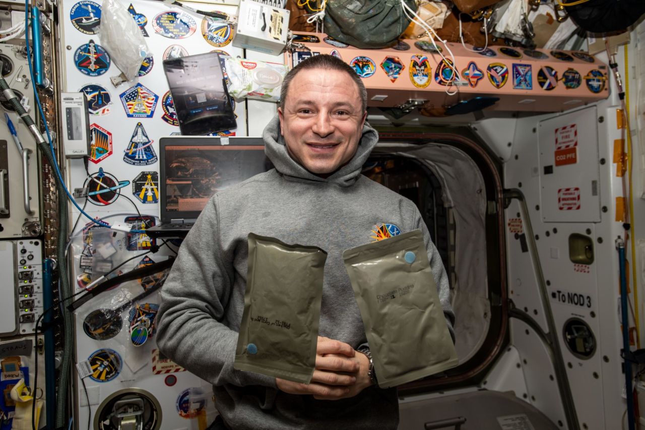 NASA astronaut and Expedition 61 Flight Engineer Andrew Morgan poses with two food packets, chicken with cornbread and chocolate pudding, during dinnertime aboard the International Space Station's Unity module, January 1, 2019.