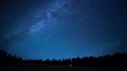 Blue dark night sky with many stars above field of trees. Yellowstone park. Milkyway cosmos background