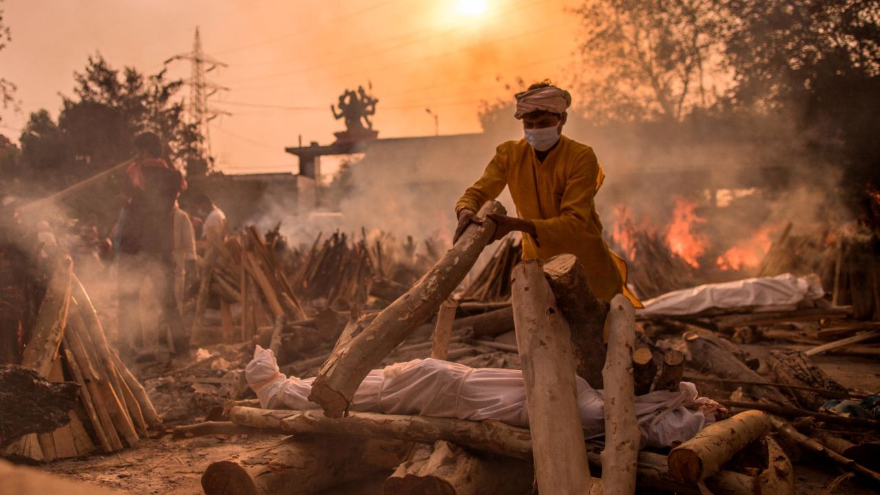 NEW DELHI, INDIA - MAY 01: A priest who works at a crematorium performs the last rites of a patient who died of COVID-19 amid burning funeral pyres on May 01, 2021 in New Delhi, India. With cases crossing 400,000 a day and with more than 3500 deaths recorded in the last 24 hours, India's Covid-19 crisis is intensifying and shows no signs of easing pressure on the country. A new wave of the pandemic has totally overwhelmed the country's healthcare services and has caused crematoriums to operate day and night as the number of victims continues to spiral out of control. (Photo by Anindito Mukherjee/Getty Images)