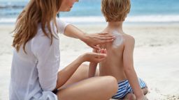 Mother applying sun cream to her son on the beach.