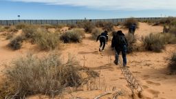 A human smuggler leads two migrants toward the wall on the US-Mexico border in Ciudad Juárez, Mexico, dragging the makeshift ladder they will use to scale the wall as they try and get into the US.