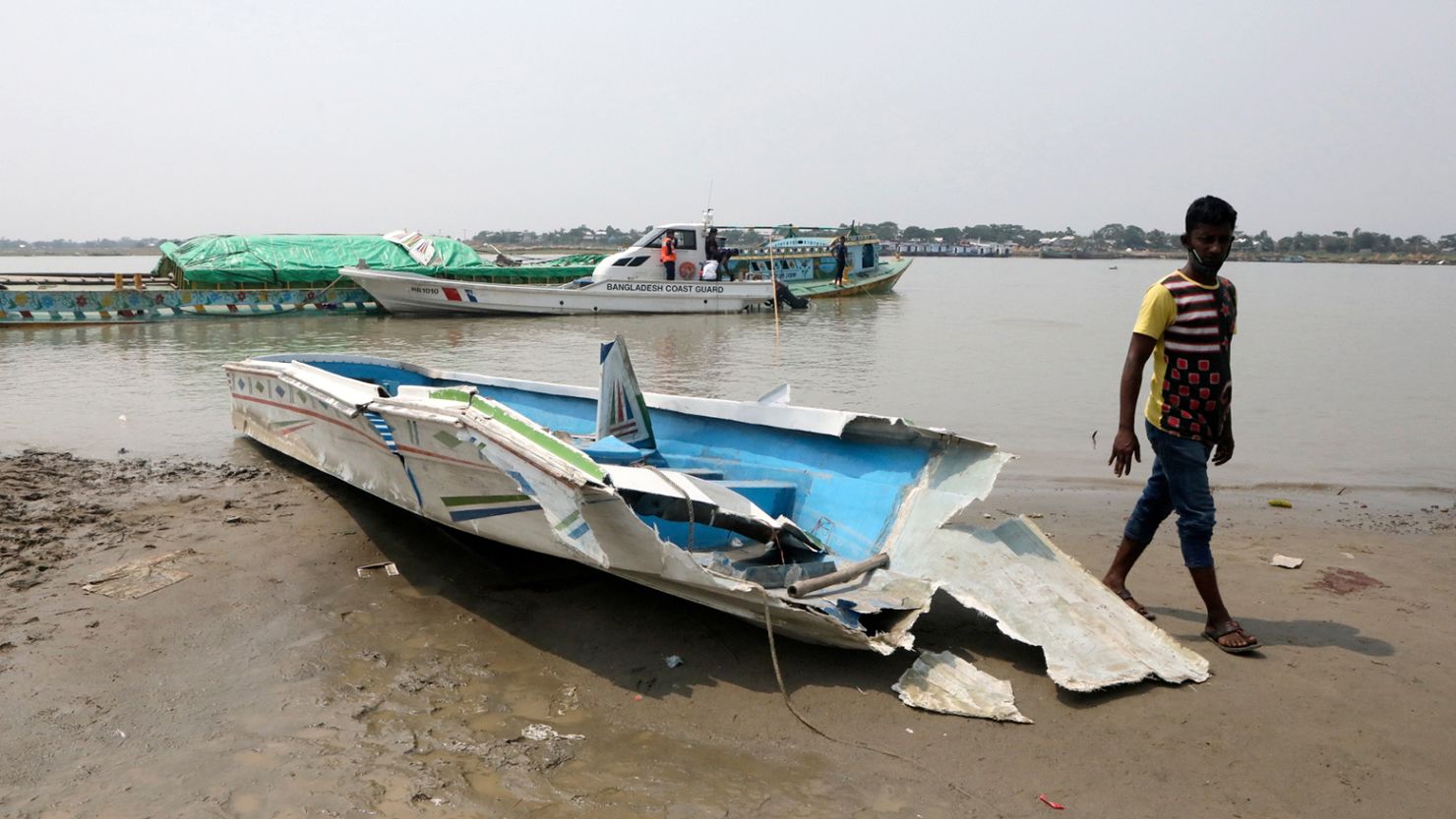 A man walks past the mangled remains of a speedboat that overturned after hitting a cargo boat in Madaripur, Bangladesh on May 3, 2021.