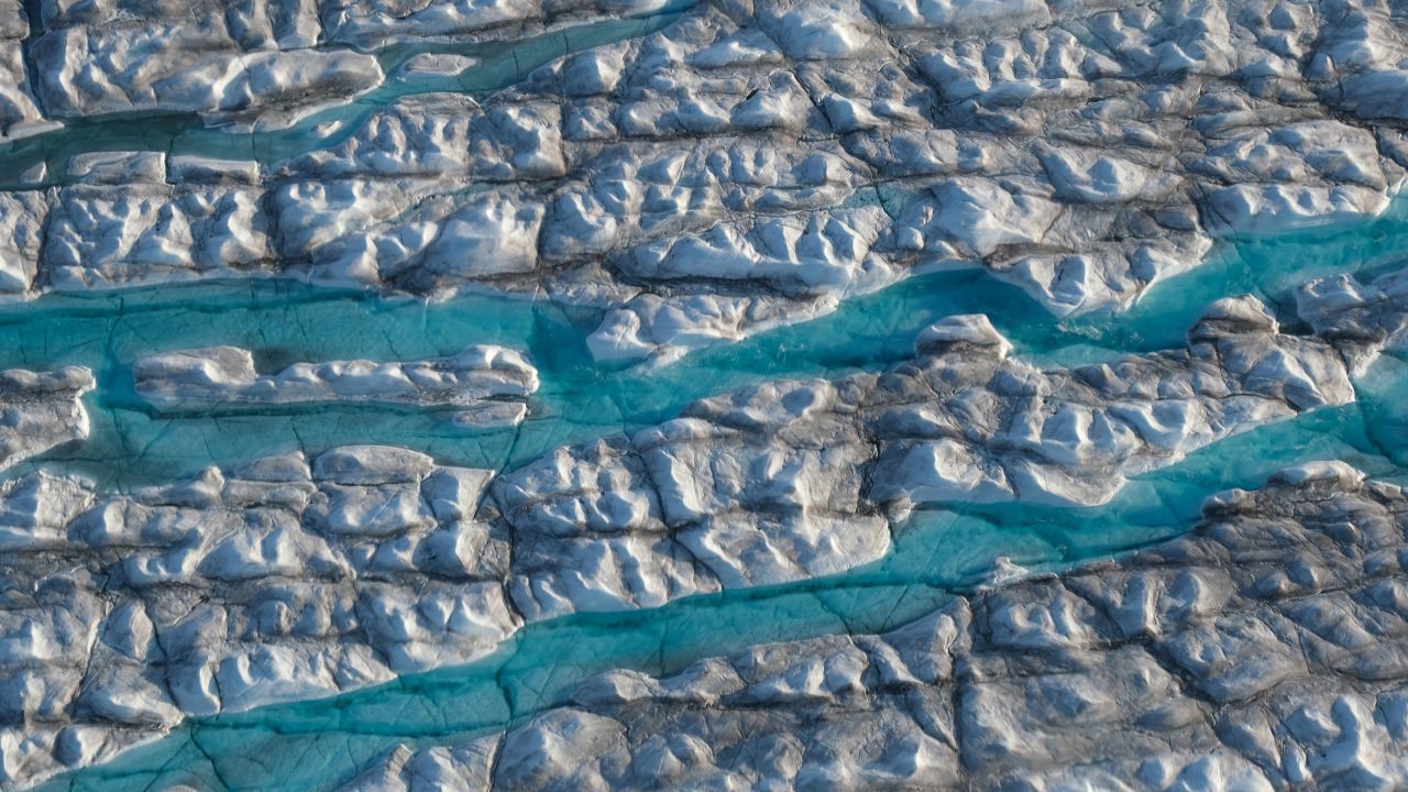 Rivers of meltwater carve into the Greenland ice sheet. A new study finds that limiting warming to below 1.5 degrees Celsius could cut sea level rise caused by melting land ice this century in half.