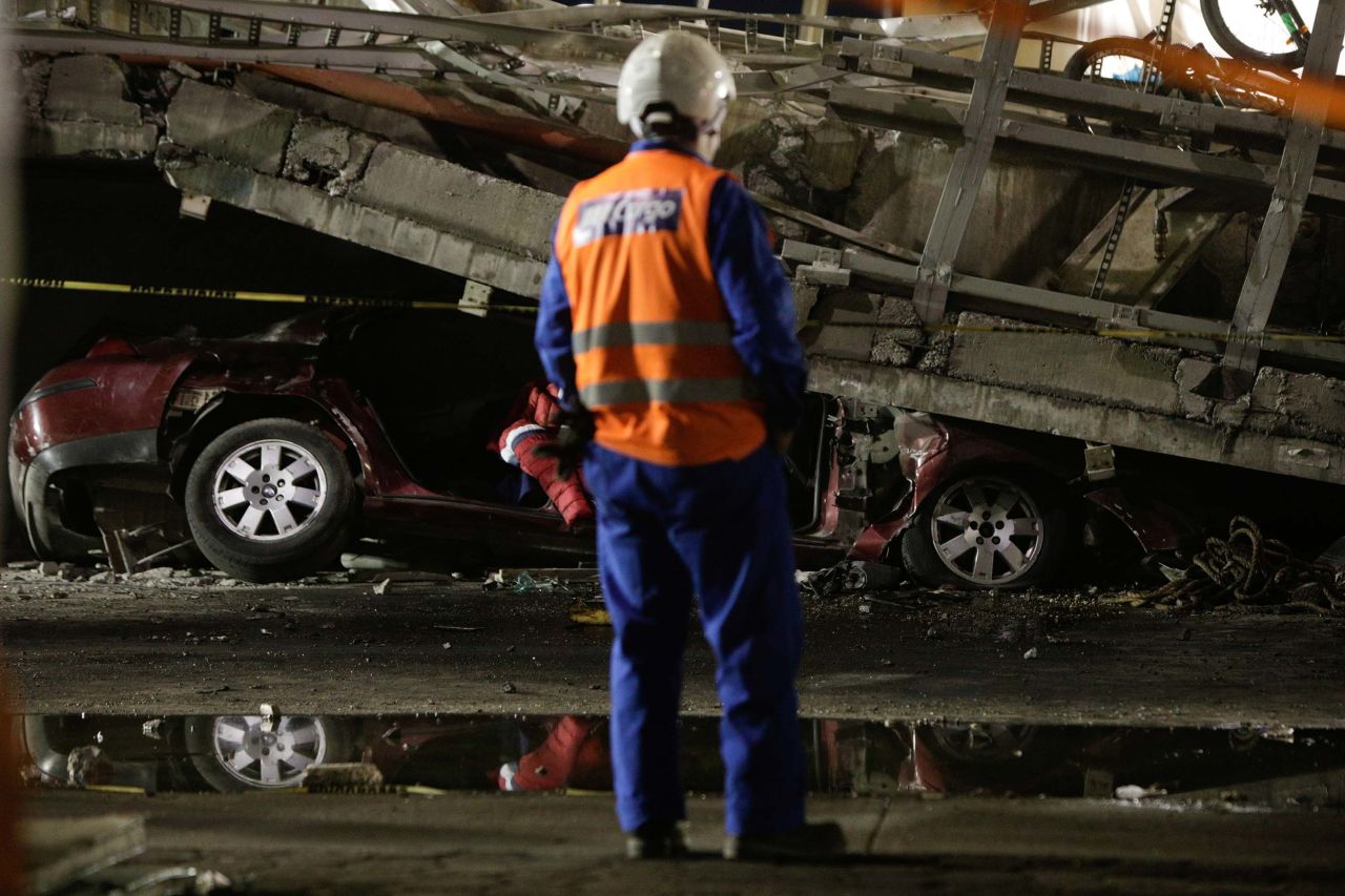 A rescue worker stands in front of a car that was trapped under the collapsed overpass.