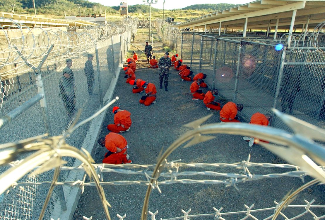 Detainees wearing orange jumpsuits are seen under guard on January 11, 2002 in a holding area at Camp X-Ray, on the US Naval Base at Guantanamo Bay, Cuba.