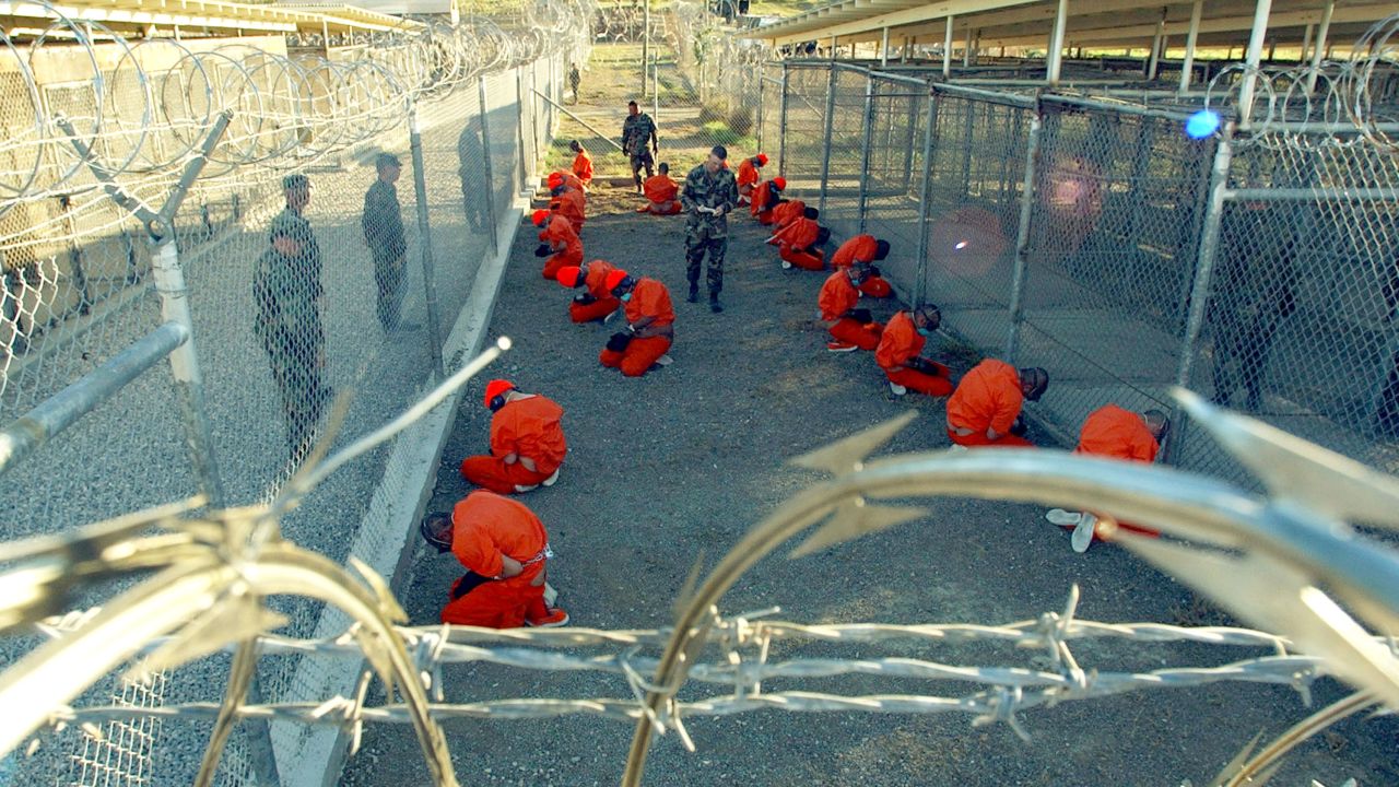 Detainees wearing orange jumpsuits are seen under guard on January 11, 2002 in a holding area at Camp X-Ray, on the US Naval Base at Guantanamo Bay, Cuba.