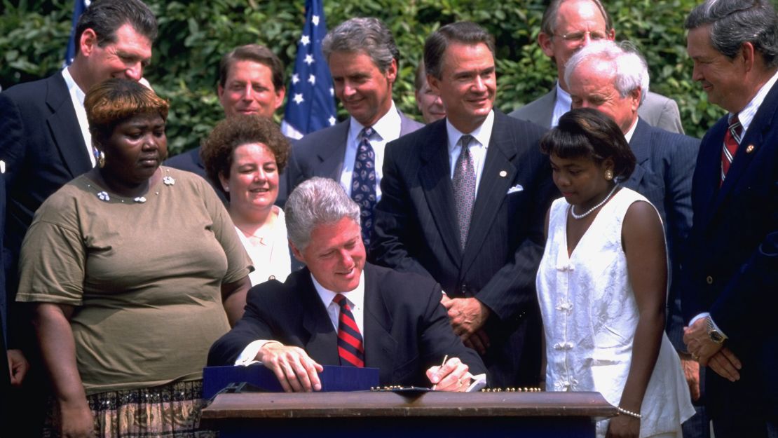 President Bill Clinton signs a controversial welfare reform bill in the White House Rose Garden in 1996 as former welfare recipients and others look on.