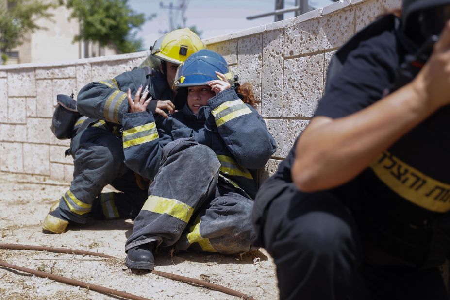 Israeli firefighters take cover in Ashkelon as a siren warns of incoming rockets on May 11.
