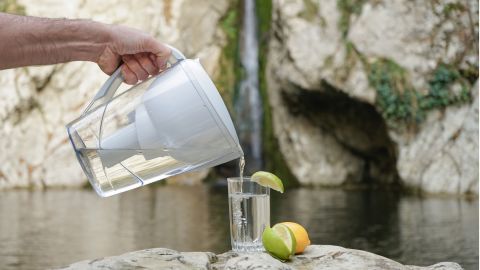 hand-pouring-filtered-water-in-the-big-glass-with-lemon-on-the-nature-picture-id1192823458